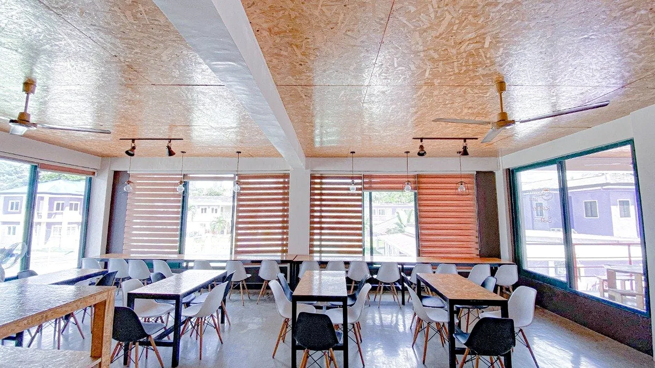 CG Academy Banilad Campusの窓の多い食堂に木のテーブルと白い椅子が並ぶ
