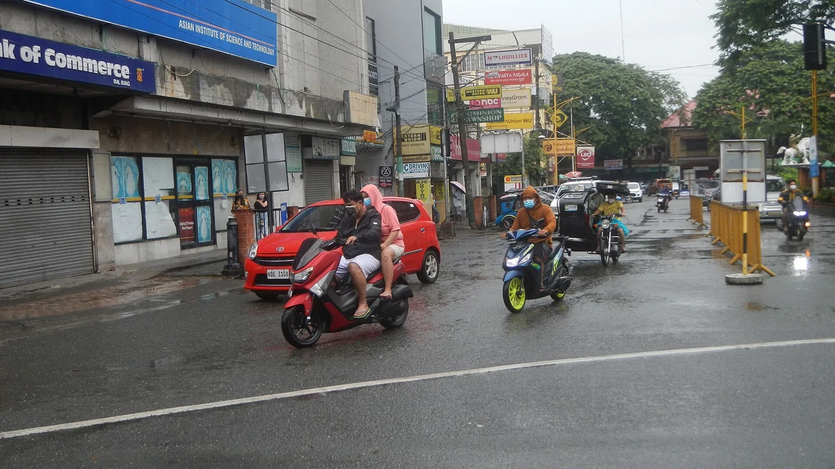 雨で濡れた道路を走るバイクと歩行者