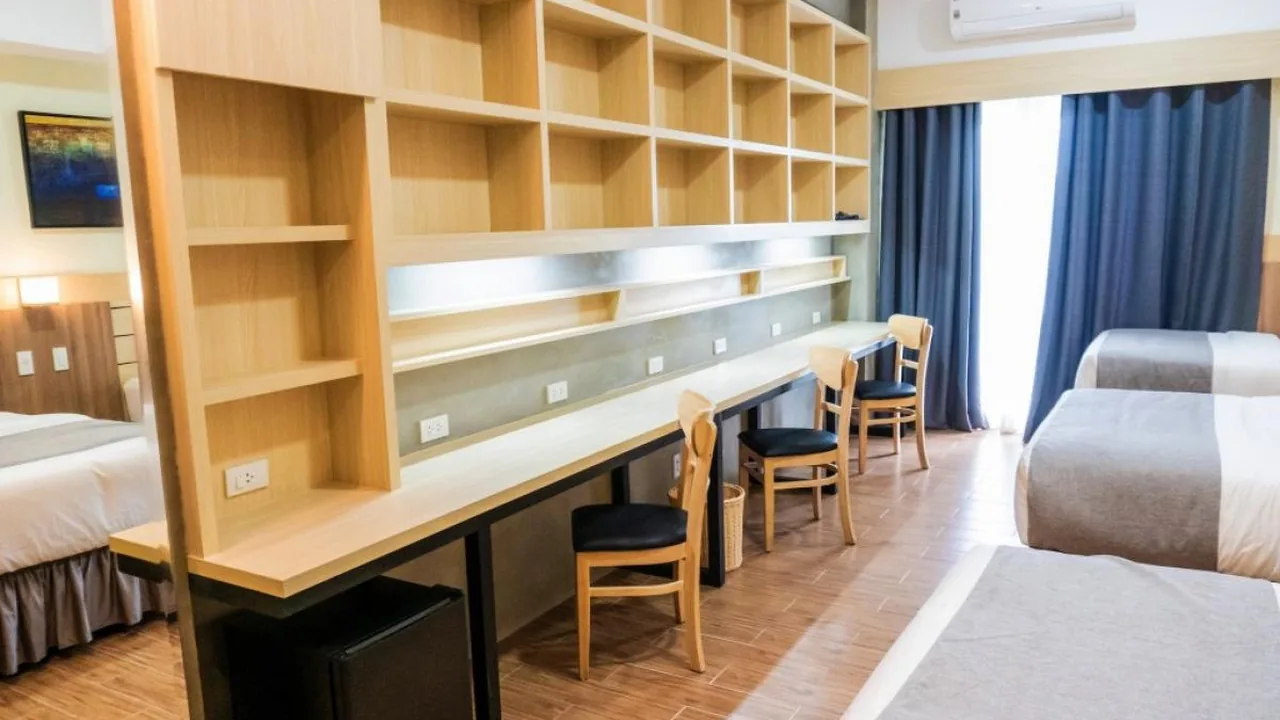 長い机と本棚が備え付けられた、ベッド3台の学生寮の部屋