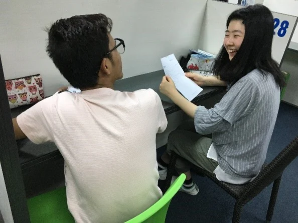 宿雾语言训练小隔间内两名学员用讲义练习口语
