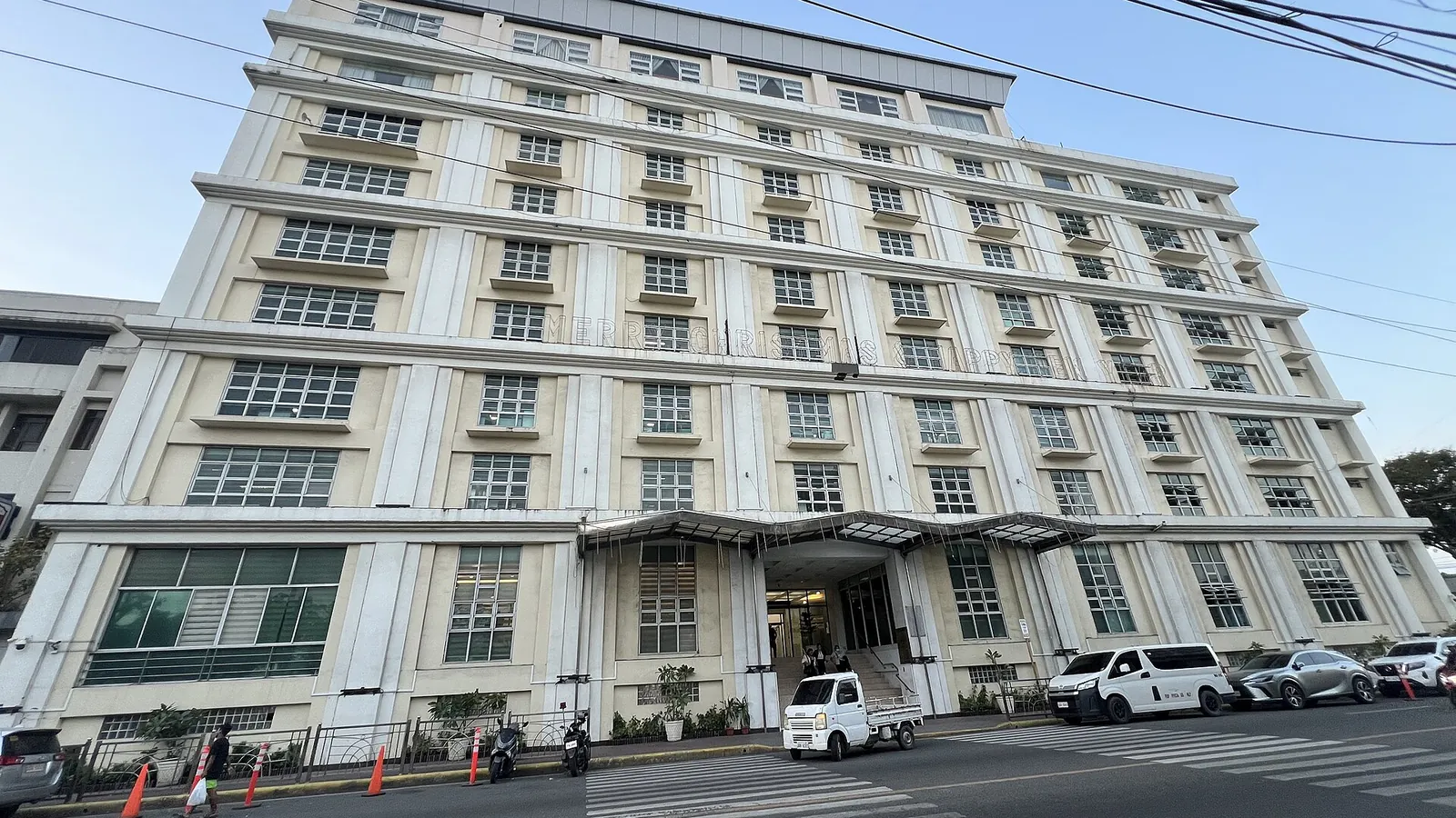 白い外壁の大きな建物と、前に止まる車