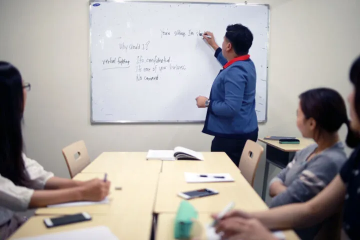 ホワイトボードに書きながら授業をする講師と学生
